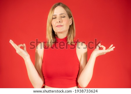 Mindful peaceful woman meditates indoor, keeps hands in mudra gesture isolated over red background.