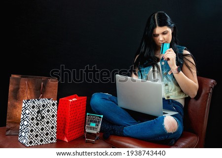young female shopping online at home sitting besides row of shopping bags, isolated on dark