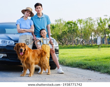 Happy family of three and pet dog in front of car in the park