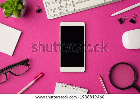 Top view photo of workplace with smartphone in the middle keyboard mouse chancellery magnifier plant glasses and notebooks on isolated pink background with copyspace