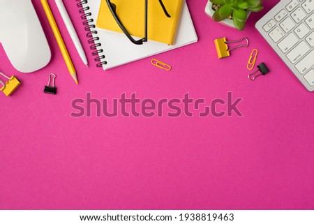 Top view photo of workplace with notepads flower keyboard mouse yellow chancellery clips binders pen and pencil on isolated pink background with copyspace