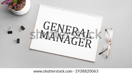 GENERAL MANAGER is written in a white notebook next to a pencil, black-framed glasses and a green plant.