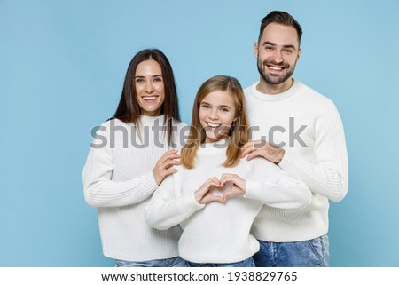 Cheerful young parents mom dad with child kid daughter teen girl in sweaters showing shape heart with hands heart-shape sign isolated on blue background studio portrait. Family day parenthood concept