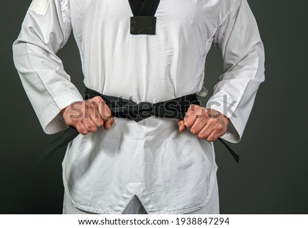 Strong male athlete in white taekwondo kimono puts on sensei black belt Royalty-Free Stock Photo #1938847294