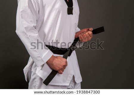 Strong male athlete in white taekwondo kimono puts on sensei black belt Royalty-Free Stock Photo #1938847300
