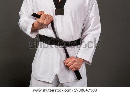 Strong male athlete in white taekwondo kimono puts on sensei black belt Royalty-Free Stock Photo #1938847303