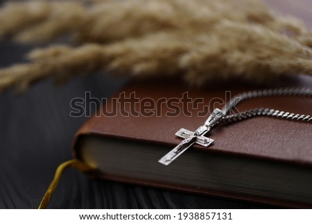 Silver necklace with crucifix cross on christian holy bible book on black wooden table. Asking blessings from God with the power of holiness, which brings luck
