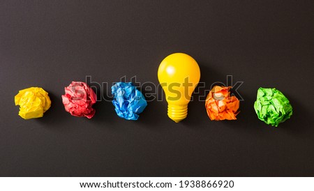 Colorful crumpled paper ball with yellow light bulb against black background.  Royalty-Free Stock Photo #1938866920