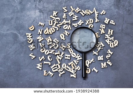 Magnifying glass with wooden alphabet on gray concrete background. Education concept. Flat lay.