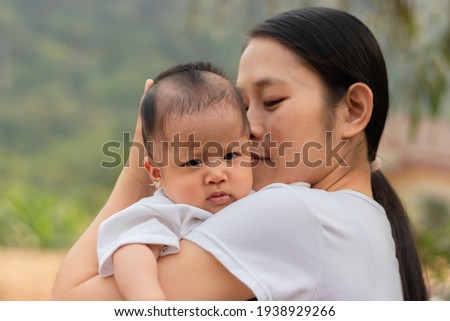 Young Asian mother kissing and holding little daughter in the park, Mother play enjoying with her cute baby girl in outdoor, copy space