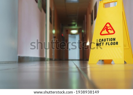 Yellow sign of slippery floor in the room after cleaning. A sign that reads Caution is a long empty industrial corridor.