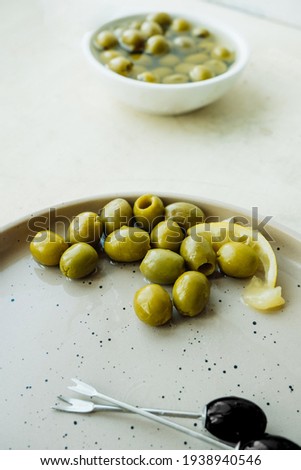 the real moment of eating green olives with lemon. A plate of olive tree fruit, snack forks, and squeezed slice of lemon. vertical content, selective focus
