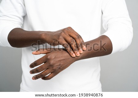 Closeup of African man arms touching painful wrist caused by prolonged work on computer, laptop. Black male suffering from carpal tunnel syndrome, arthritis, neurological disease. Numbness of hand.
