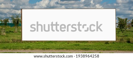 Large long billboard stands on lawn with green grass at city neighborhood. Advertising and announcement concept.