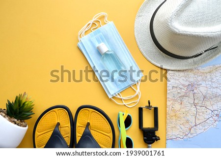 Travel kit (hat, map, antibacterial Gel, medical mask,monopod, passport) on a yellow background. Travel flat lay.Planning a summer vacation