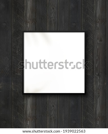 Black square picture frame hanging on a black wooden wall. Blank mockup template
