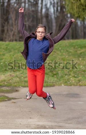 A girl with glasses rides roller skates. Seasonal outdoors children activity sport. The girl jumps with roller skates