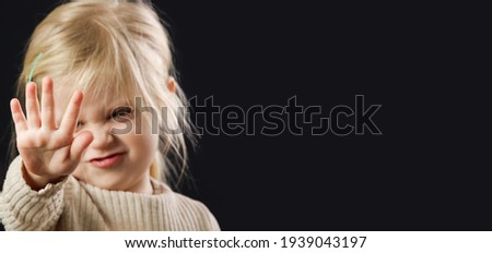 Toddler girl showing open palm as a stop hand gesture. Studio portrait on black background with copy space.