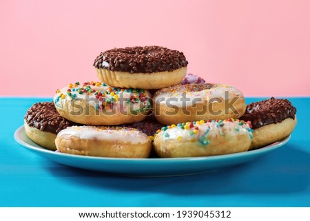Breakfast time. Close up of various colourful round glazed donuts with sprinkles on the plate over blue and pink background. Desserts, dieting and junk food concept