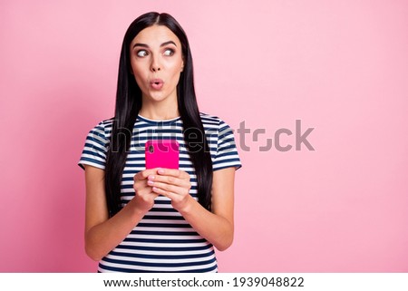 Photo portrait of shocked girl looking at blank space holding phone in two hands isolated on pastel pink colored background