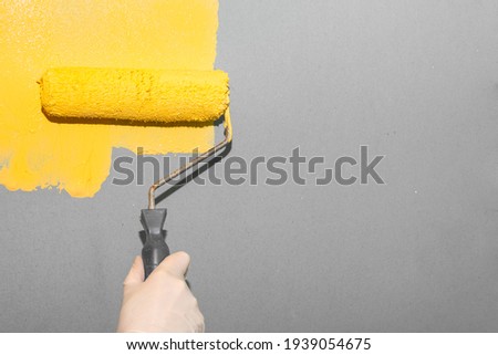 Painting work. A woman paints a gray wall with a roller yellow. Trending colors of the year. Royalty-Free Stock Photo #1939054675