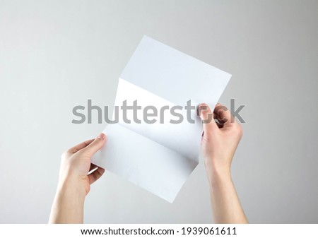 Hands hold a white three fold flyer. A clean flyer in your hands. For your text. Isolated on a gray background.