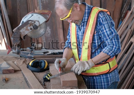 Half body shot: Carpenter working hand to measure lumber with a metal ruler and pencil to mark in a woodworking factory. There is many craft equipment such as electric saw, tape measure, etc.