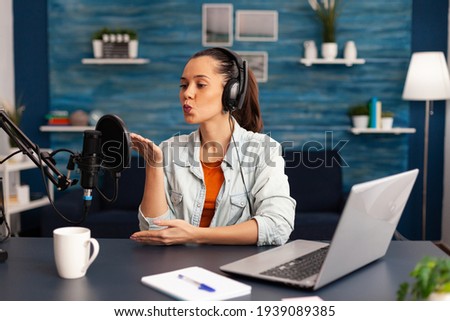Vlogger giving flying kiss while making daily online video blog. Digital influcencer recording talk show at home studio brodcast using headphones, professional podcast microphone and modern laptop