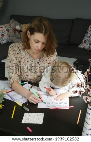 Adorable little girl coloring picture for Easter at home with her mum. Family craft activity with toddlers.