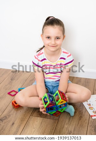 Kid plays with a magnetic constructor toy. A little child girl is playing with colorful blocks. Heart from a magnetic constructor. 