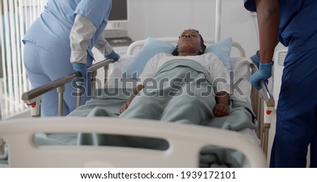 Medical team push emergency stretcher transporting afro woman patient in hospital. Sick unconscious female lying in hospital bed moved by doctors in hospital ward Royalty-Free Stock Photo #1939172101