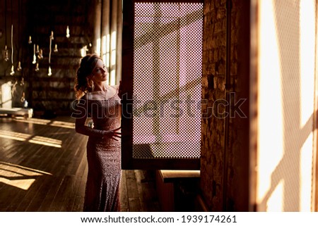 a girl in a lace dress stands at the window with open shutters