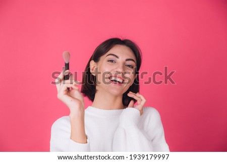 Woman in casual white sweater on pink red background with makeup on face hold blush brush isolated copy space beauty portrait