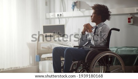 Young disabled afro-american man sitting in wheelchair in hospital ward. Portrait of upset and frustrated african patient in wheelchair after serious injury in modern clinic Royalty-Free Stock Photo #1939180168