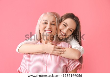 Portrait of young woman and her mother on color background Royalty-Free Stock Photo #1939199056