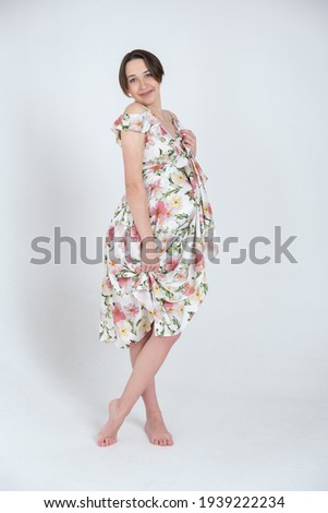 Studio portrait of cheerful young pregnant woman in summer dress on white grey background, happy pregnancy concept