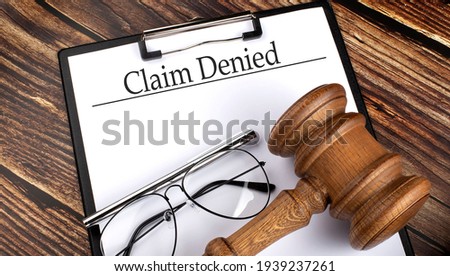 Paper with CLAIM DENIED with gavel, pen and glasses on wooden background