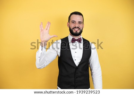 Young man with beard wearing bow tie and vest doing hand symbol