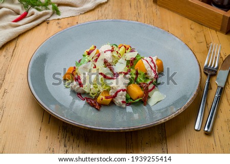 salad with pumpkin, cheese and herbs on grey plate on wooden table