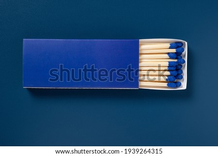 blue matchbox and blue match sticks on a black background Royalty-Free Stock Photo #1939264315