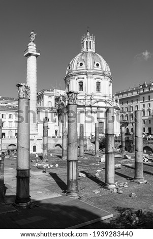 Black and white photo of ruins of ancient roman columns standing in front of exterior facade of catholic church in Italy