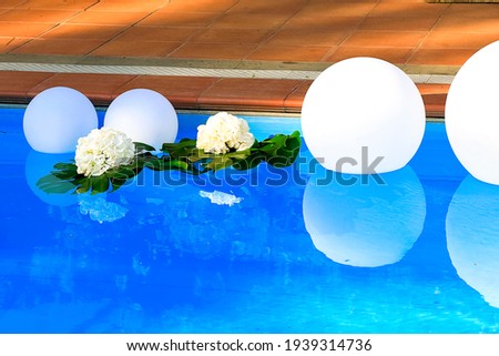 Swimming pool border decorated with white floating balls and fresh flowers for wedding party. Summer event preparation. Party design. Clean transparent blue water. Background and postcard picture 