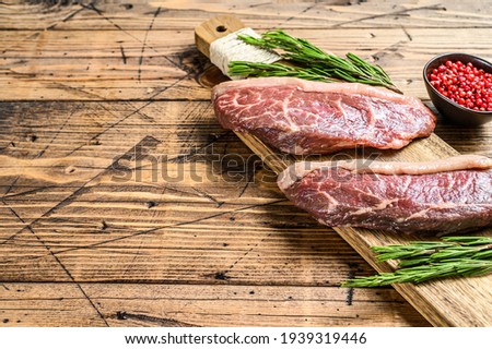 Raw rump cap steak on a chopping Board. wooden background. Top view. Copy space