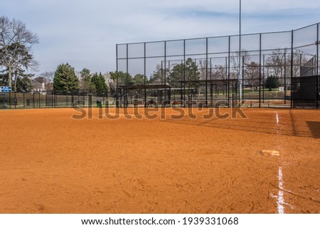 Empty baseball field at a local park opened for practice standing behind third base looking towards home plate with the fence and bleachers in the background on a warm sunny day in early spring