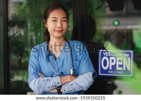 Veterinarian doctor in blue suit with a stethoscope. Asian woman vet Smiling, arms crossed standing on animal hospital. Portrait confident female veterinary with open shop sign for examining puppy dog