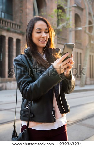 vertical photo of a smiling young woman reading a message at her telephone at the street, concept of technology and communication, copyspace for text