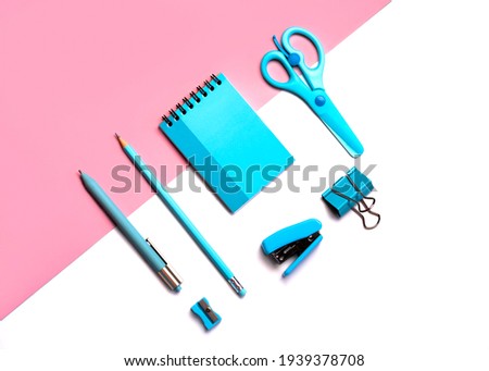 Flat Lay top view  of scissors, pencil, paper clips,stapler,pencil sharpener, pen with blue note pad on a pink and white background.School stationery concept
