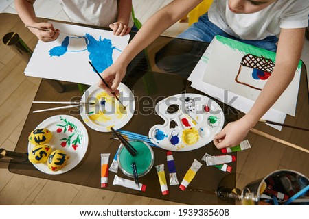 Hands of kids drawing with watercolor paints on paper. Children creativity concept. High angle view
