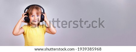 A narrow photo of a cute little girl in big headphones on a gray background.