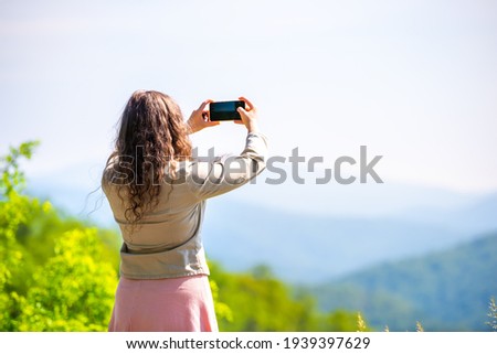 Young woman standing taking selfie photo picture of overlook in Shenandoah Blue Ridge appalachian mountains with bokeh background of peak